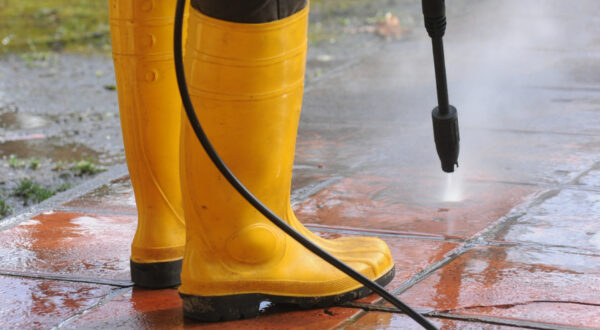person-wearing-yellow-rubber-boots-with-high-pressure-water-nozzle-cleaning-dirt-tiles